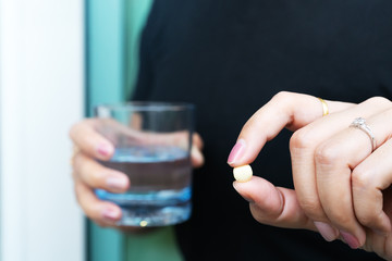 medicine, health care and people concept - close up a pill on woman hand