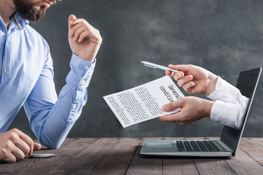 Businessman Reads General Conditions Presented By Hands Coming Out Of A Laptop. Metaphor For Signing Contracts Via The Internet