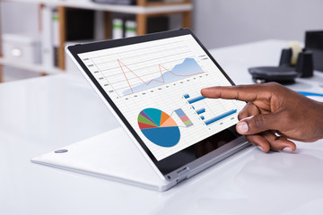 Man's Hand Pointing On Graph At Laptop