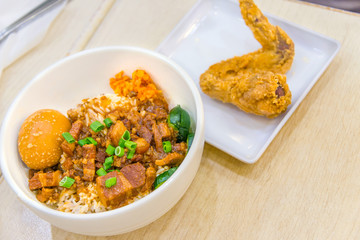 Braised pork rice and egg and in sweet brown sauce with fried chicken wings delicious food in Singapore on wooden table