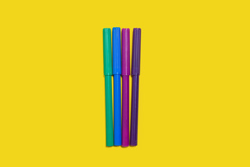 four new bright plastic colored felt pens lying on a yellow surface. concept of office supplies