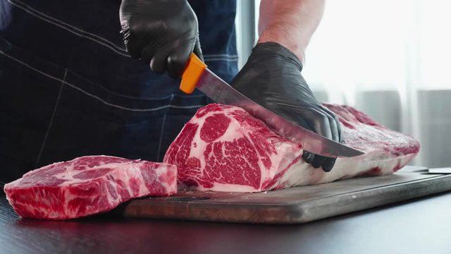 Chef cuts raw meat on the wood board with the knife, close-up