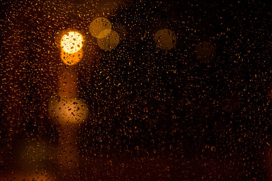 Rain drops on the window. Rain drops on the glass on a background of a night blurred city. Rainy weather. Outside the window is a blurred city. Bokeh night city.