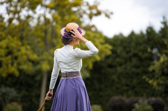 Beautiful girl in a vintage dress. Girl on a blurred background. A girl in a white blouse and a purple dress. A woman is dressed in retro style. The girl is straightening the hat on her head.