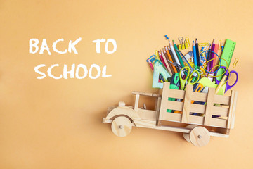 Back to school concept with wooden toy truck with school supplies on yellow background.