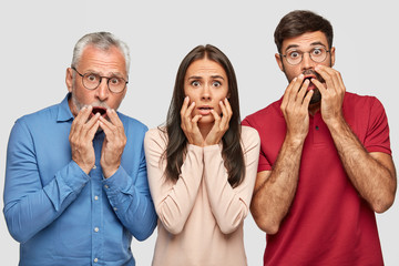 Three shocked people pose indoor. Surprised brother, sister and their elderly father stare with...