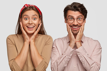 Amazed beautiful young European female and handsome bearded guy keep hands under chin, smile...