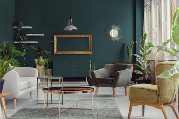 Armchairs and couch next to copper table in green apartment interior with mockup of frame. Real photo - obrazy, fototapety, plakaty