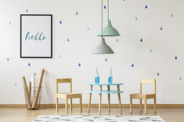 Small wooden chairs and table set for kids and mock-up poster on a white wall with wallpaper in a preschool room interior with blue and green elements
