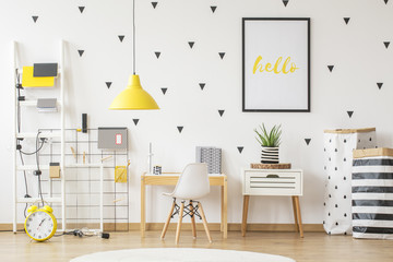 Small wooden desk and a modern chair for a young pupil and creative, vibrant yellow decorations in a scandinavian style child bedroom interior with white walls © Photographee.eu