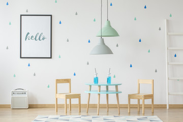 Cute, wooden furniture for children and a mock-up poster on a white wall with blue and green droplets in a modern kid playroom interior