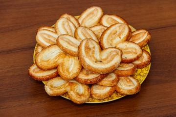 Palmier biscuits - french cookies made of puff pastry (also called palm leaves, elephant ears or french hearts) in a plate on wooden table