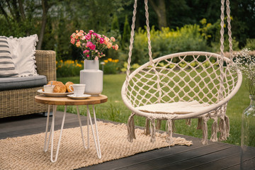 Hanging chair next to table with flowers on terrace in the garden during spring. Real photo