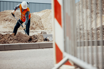 Craftsman in reflective vest and white helmet digging in sand