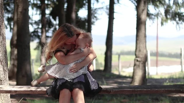 Slow otion mother holding little girl in her arms. Sitting on wood bench in the forest. Parent protecting child