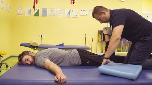 Doctor physiotherapist helping young disabled sportsman, doing leg exercises at the rehabilitation center. Health reductive gymnastics.