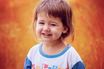 Little unkempt baby girl smiling on an orange background, open air