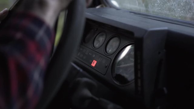 Outdoorsy man arms on the wheel driving a vintage 4x4, focus on instrument panel, handheld