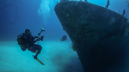 An underwater photographer takes position in front of the bow of a sunken patrol boat.