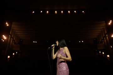 Beautiful singer against the auditorium. Back view girl in long gown performing on stage.