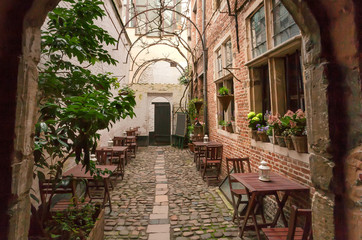 Fototapeta na wymiar Cozy outdoor cafe in old style narrow street with tables, brick walls, wooden furniture and cobbled stones
