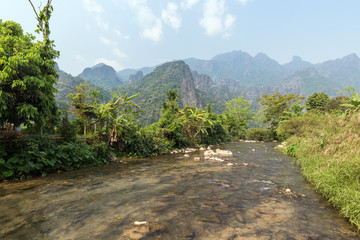 Beautiful view of a small and shallow river and striking karst limestone mountains near Vang Vieng, Vientiane Province, Laos, on a sunny day.