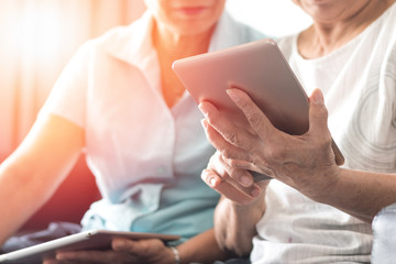 .Happy elderly twin senior people society lifestyle concept. Ageing Asia women using tablet share social media together in wellbeing county home.