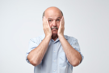 Bald mature man with mustache in blue shirt is suffering from indecision.