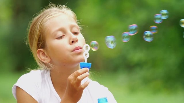 nine-year-old girl plays with soap bubbles in the summer garden.
