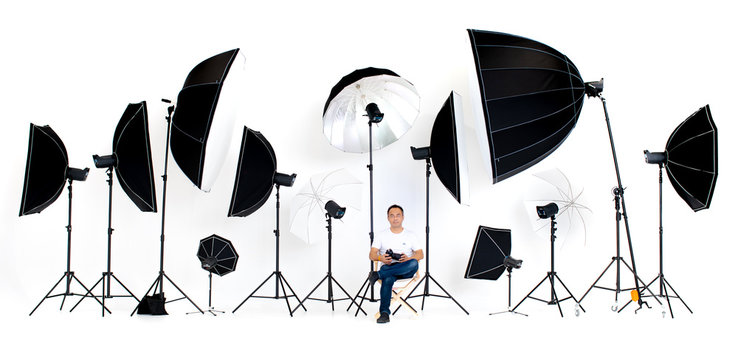 Asian photographers sit on the director's chair with flash studio lights a lot of patterns around on white background.