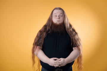 The big bearded red-haired man. Photo of a fat man in a studio on a yellow background.