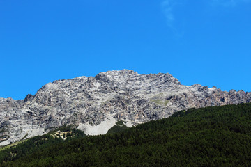 Mountain without snow partially covered by a forest against clear blue sky in summer
