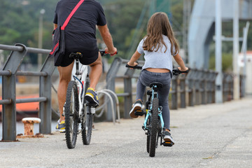 father and daughter ride bikes, rear view