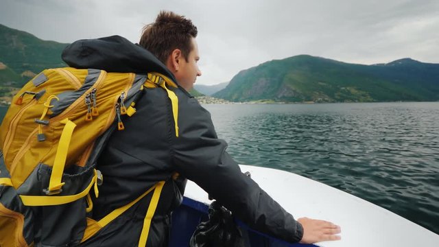 A man traveler stands on the nose of a small cruise ship, sails on a picturesque fjord in Norway