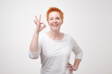 Fototapeta premium Smiling mature lady in white t-shirt gesturing perfect sign