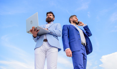 Always in touch. Men well groomed businessman holds laptop partner speak phone blue sky background....