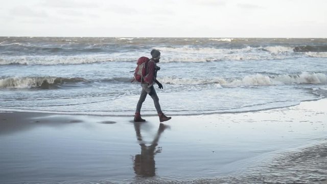Outdoorsy photographer with a backpack walking by a stormy sea, slow motion, gimbal tracking shot