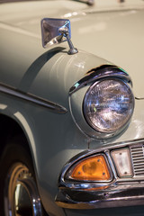 Vintage restored classic car close-up. Sealed-beam retro headlamp. Sixties headlight and wing mirror on old rusty collectors automobile.