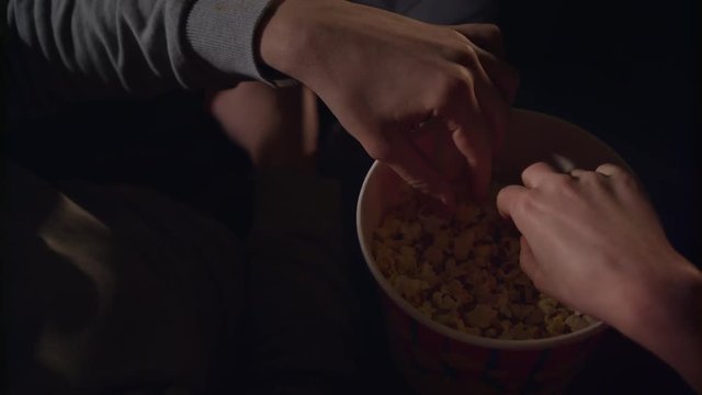 Female and male hand take popcorn grains from popcorn box in slow motion. Young couple hands eating popcorn in cinema movie. Young people eating pop corn from paper box