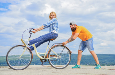 Obraz premium Woman rides bicycle sky background. Man helps keep balance and ride bike. How to learn to ride bike as adult. Girl cycling while boyfriend support her. Cycling technique. Learn cycling with support