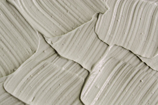 Gray cosmetic clay (kaolin) texture close up, selective focus. Abstract background with brush strokes. 