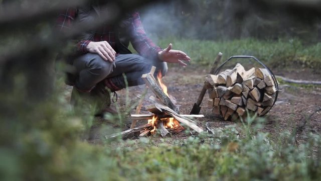 Outdoorsy man warming hands by a camp-fire in forest