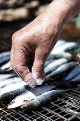 old woman salting some sardines in a grill