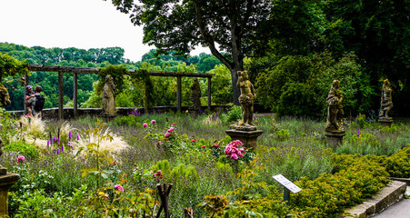 Obraz premium Beautiful public garden full of roses and statues, with an old stone wall along the outside. 