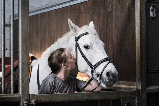 Teenage girl horserider with a grey horse outside astable, adjusting the girth and saddle.