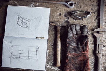 Still life of artisan metalworker's tools, sketches in a notebook and a blackened thick protective glove