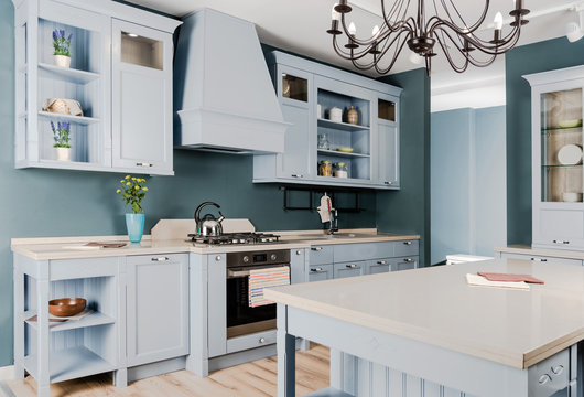 Interior Of Modern Light Kitchen With White Wooden Furniture, Potted Plants And Chandelier