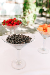 Blueberries in transparent martini glass in focus and blurred strawberry and peaches in glasses. Standing on wedding table