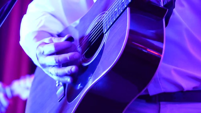 man plays an acoustic six-string guitar on stage during a performance, close-up