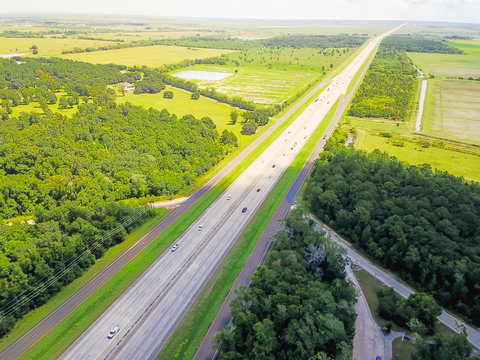 Aerial horizontal panorama view of endless Interstate 10 highway running through scenery of the Southern United States. Straight road flyover surrounded by green oak trees under cloud blue sky